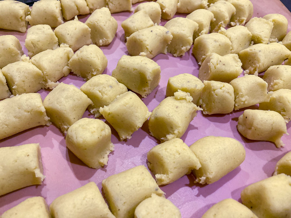 Gnocchi dough cut into pieces resting on a pink baking sheet
