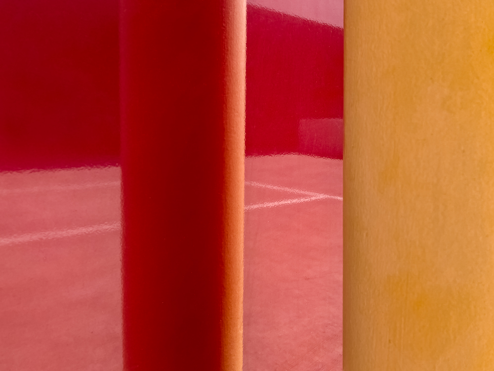 Red reflections of a car park next to a yellow bollard