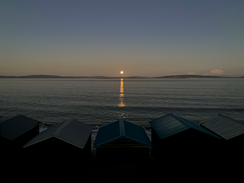 A full moon rising over a series of beach huts