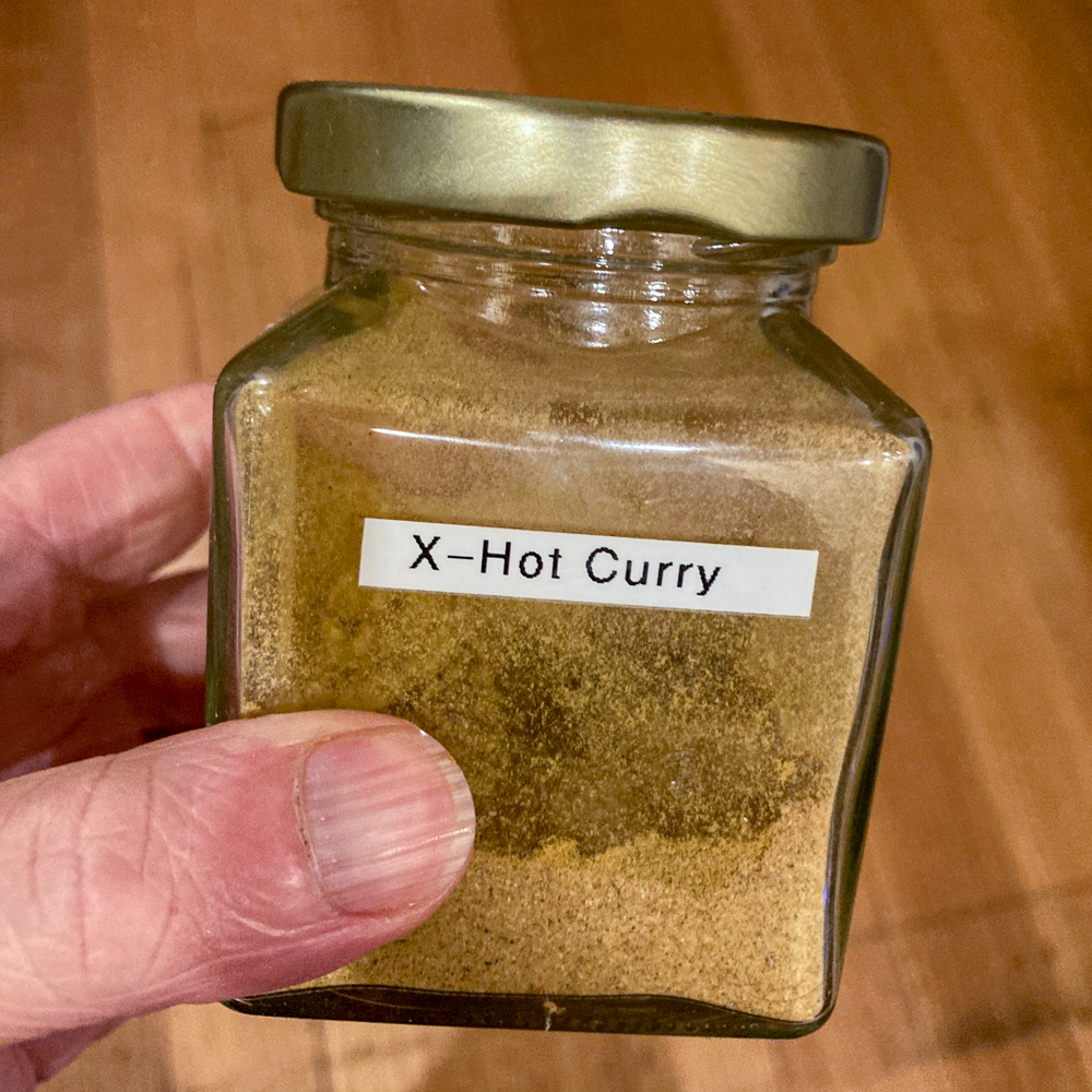 A hand holding a jar of powder labelled "X-Hot Curry"