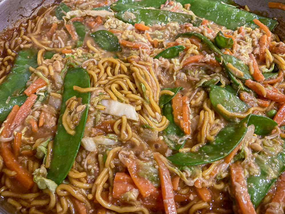 A dish of noodles with snow peas, carrots and other vegetables