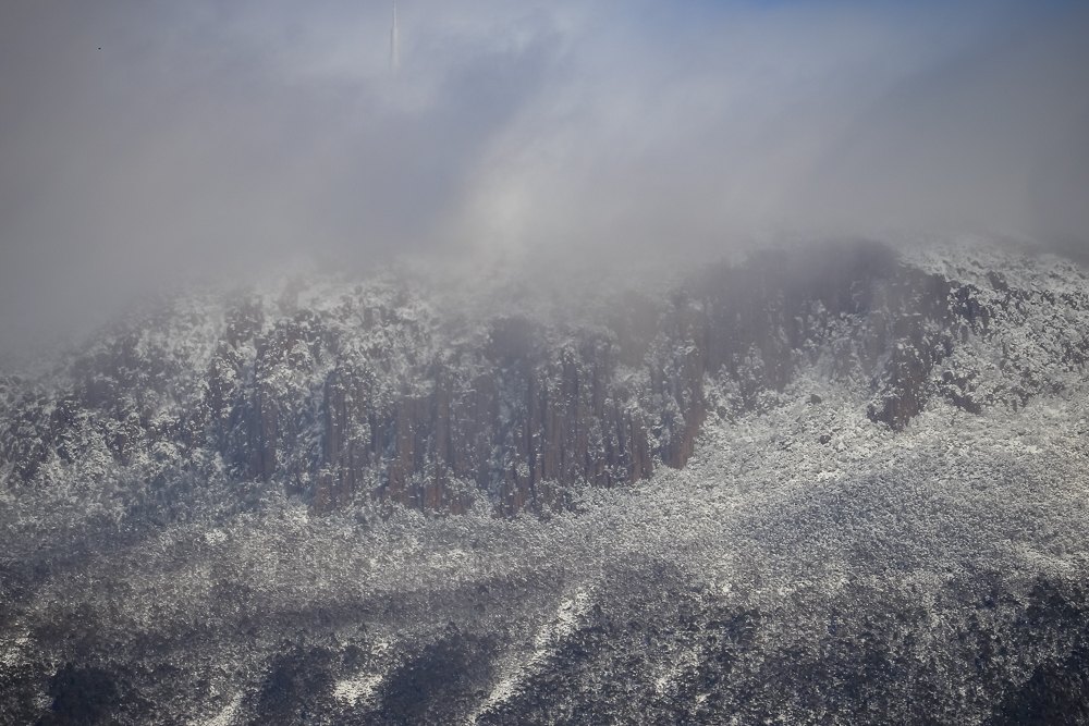 A close-up photo of kunanyi covered in snow and low cloud