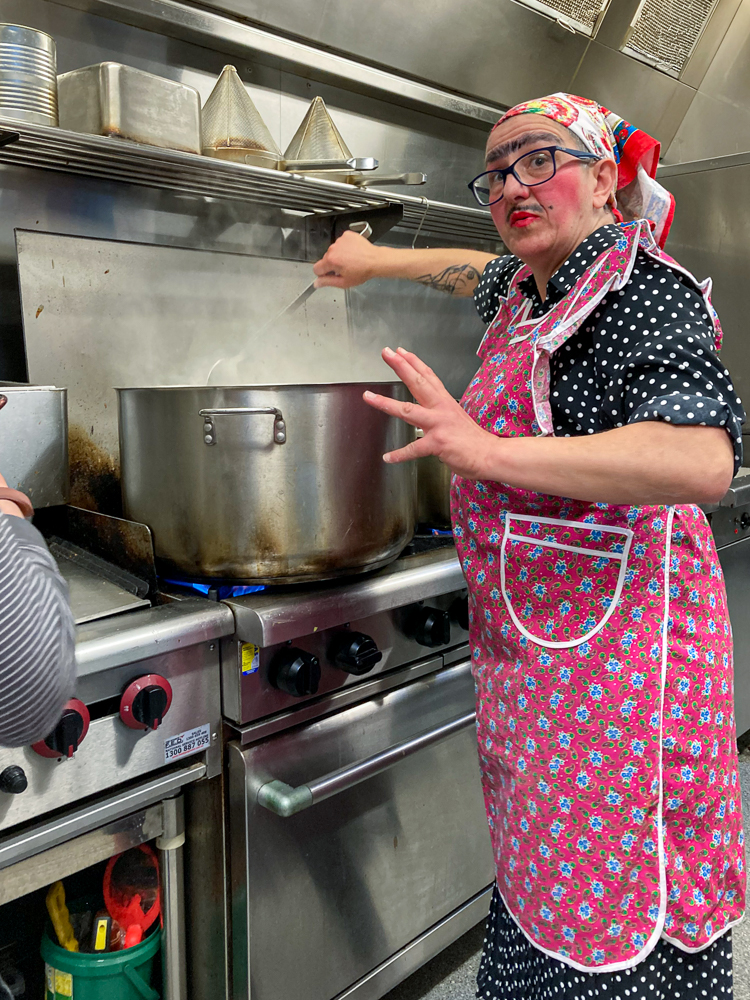 An Italian lady in a red apron cooking a giant pot of gnocchi 