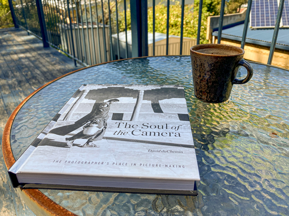 A copy of The Soul of the Camera by David duChemin on a table outside, with a cup of coffee
