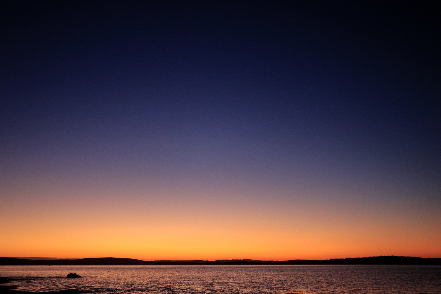 A cloudless sunrise sky above the river with tones of blue and orange