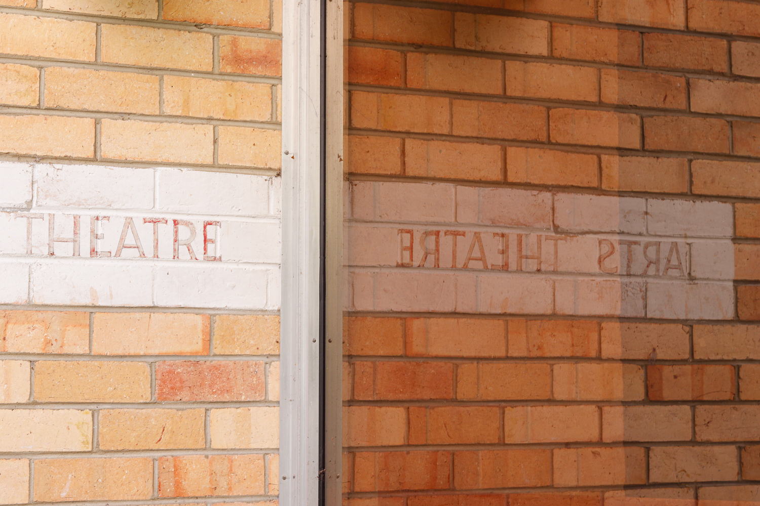 An orange brick wall with the words Arts Theatre reflected in glass