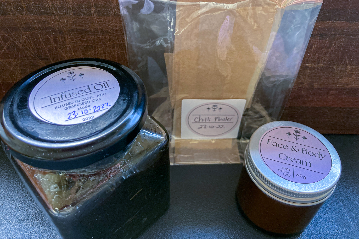 Two jars and a plastic bag. The bag contains a brown strip of kitchen paper labelled chilli plaster, the large jar is infused oil and the small jar is face & body cream