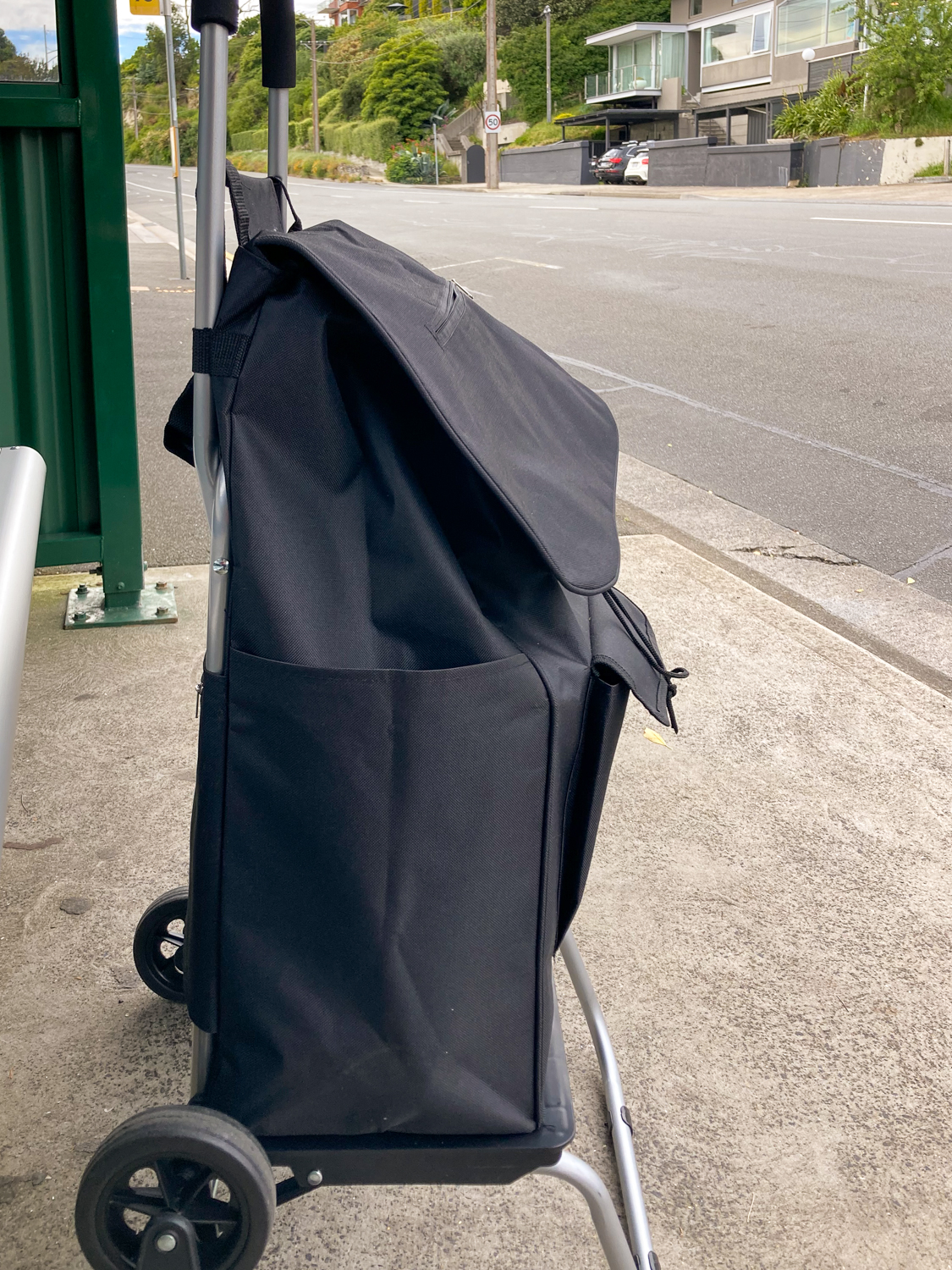 A black wheely shopping bag at a bus stop
