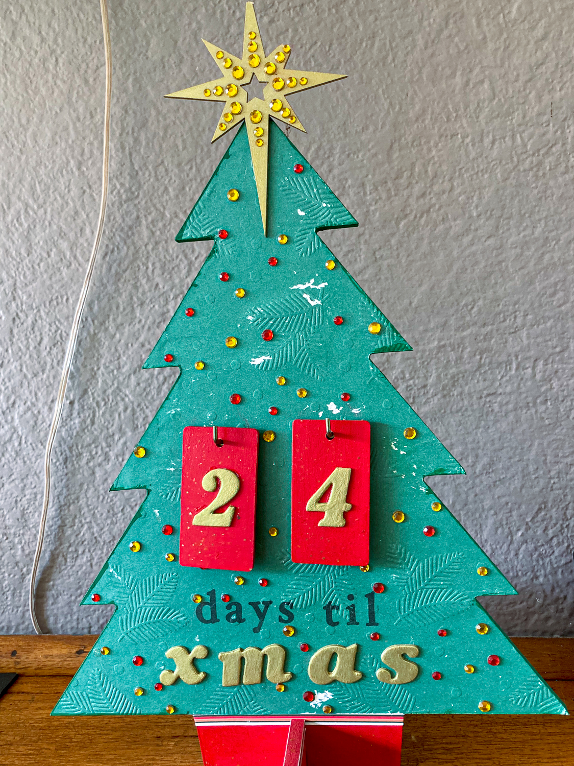 A wooden christmas tree with a gold star on top and the words "24 days til xmas"