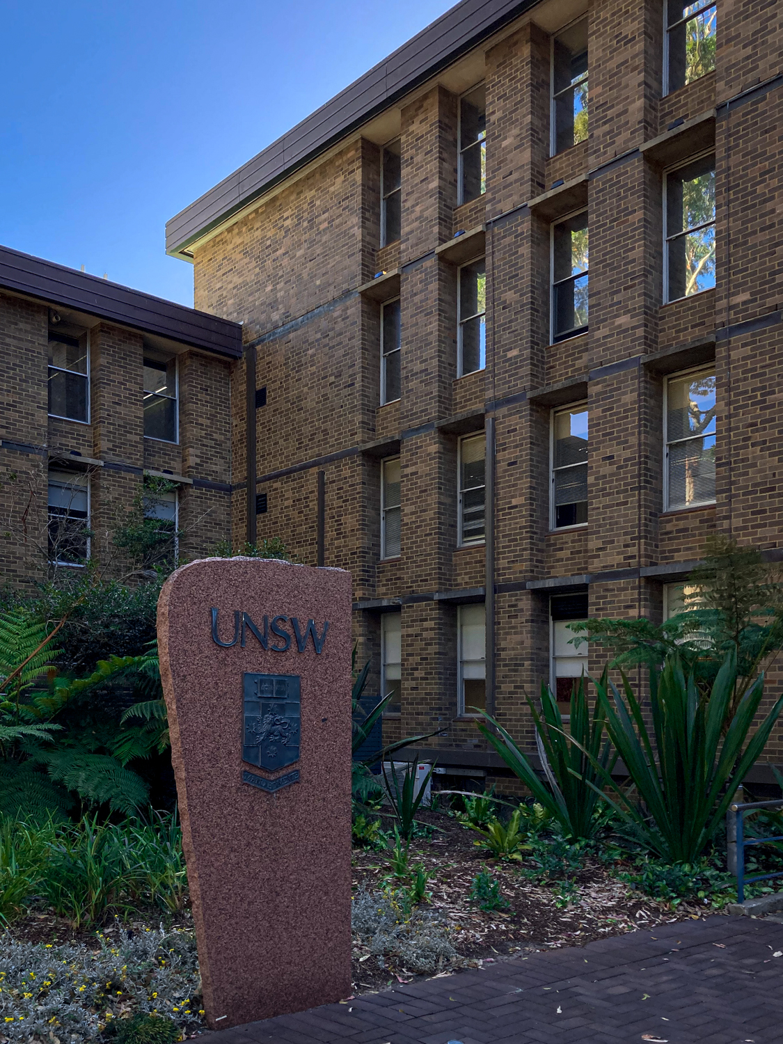 A large monolith with UNSW logo outside a four-storey brown brick building