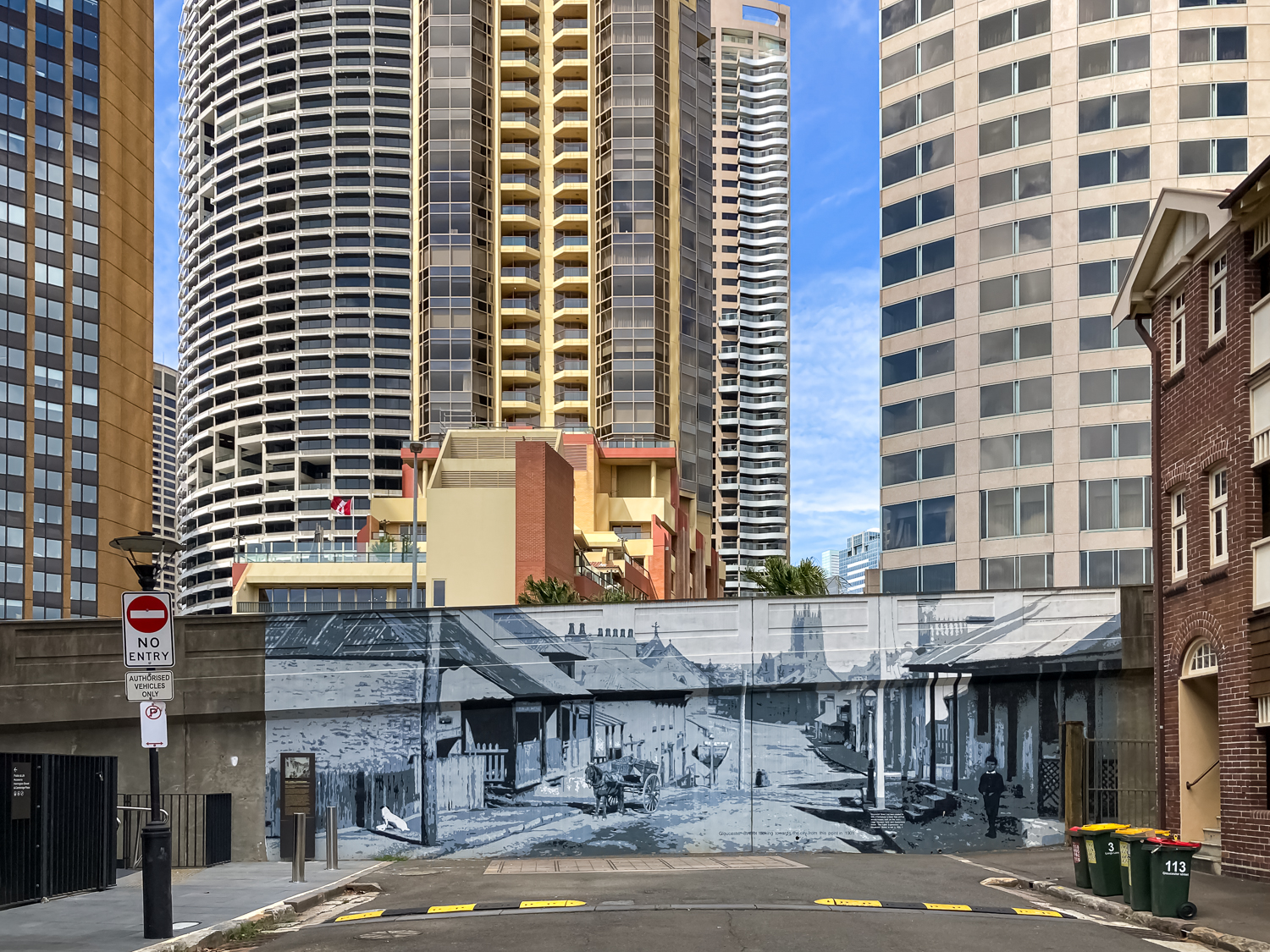 A large streetscape mural painted on the side of a freeway wall, with skyscrapers in the background
