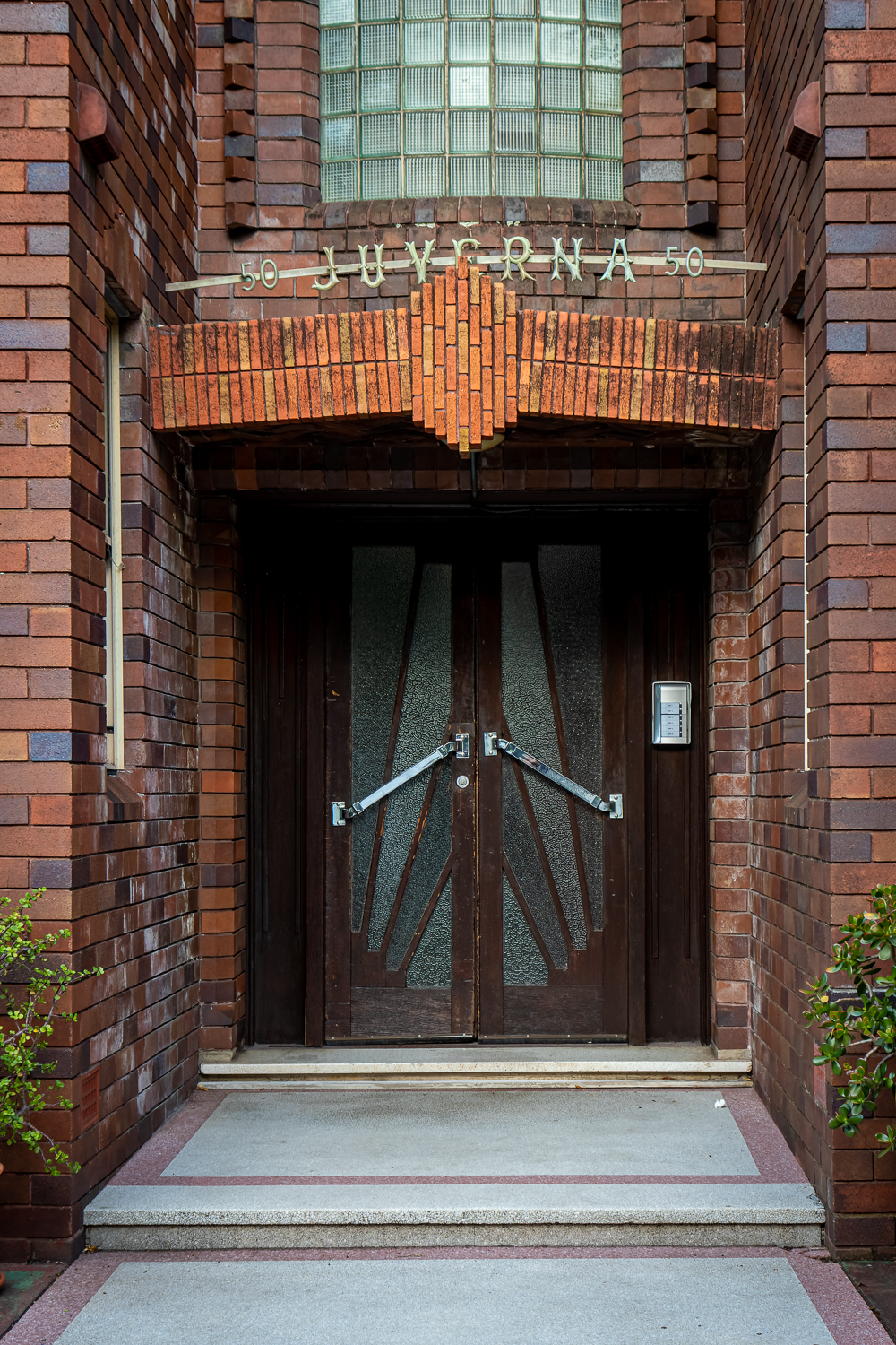 A wooden art deco door withi a red brick doorway with the word Juverna along the top
