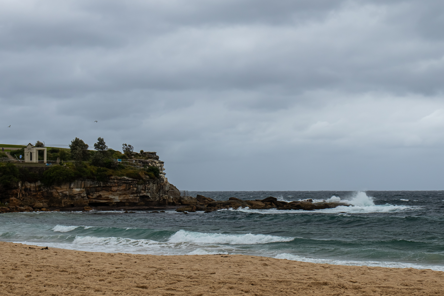 A beach and a small cliff with a small wave, on an overcast day
