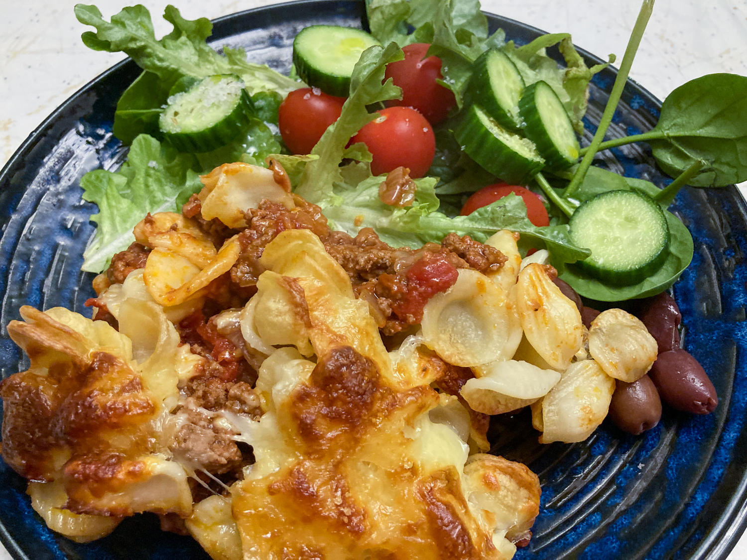 A baked pasta dish with a side salad of leaves, baby tomatoes and sliced cucumber