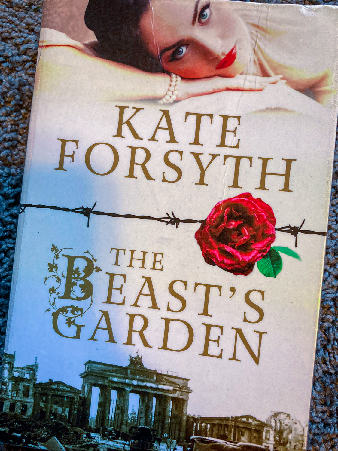 A book cover with the text Kate Forsyth The Beast's Garden. A dark-haried woman at the top, a red rose on barbeed wire across the centre and a scene from Berlin's Brandenburg Gate at the bottom
