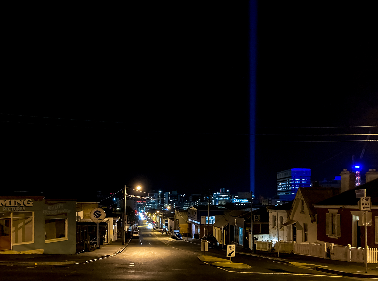 A lit city street with a large blue light beam extending into the sky