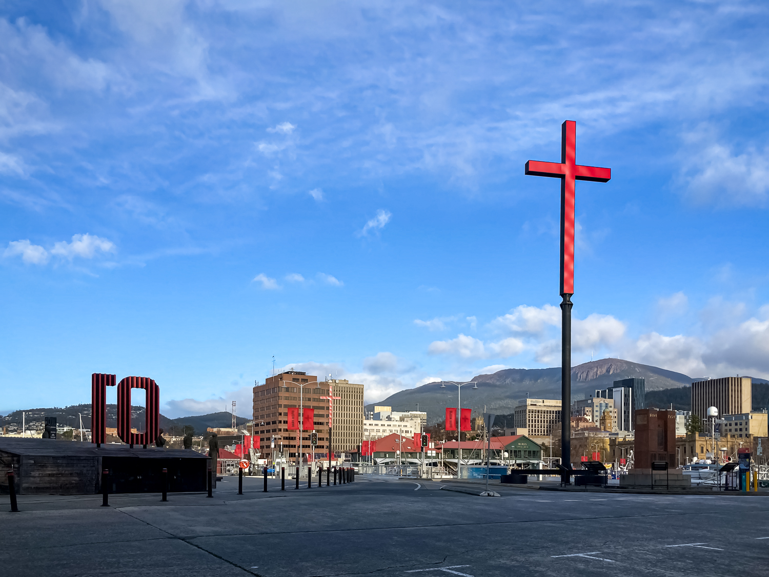 A large red cross on a black pole stand out in front of waterfront buildings