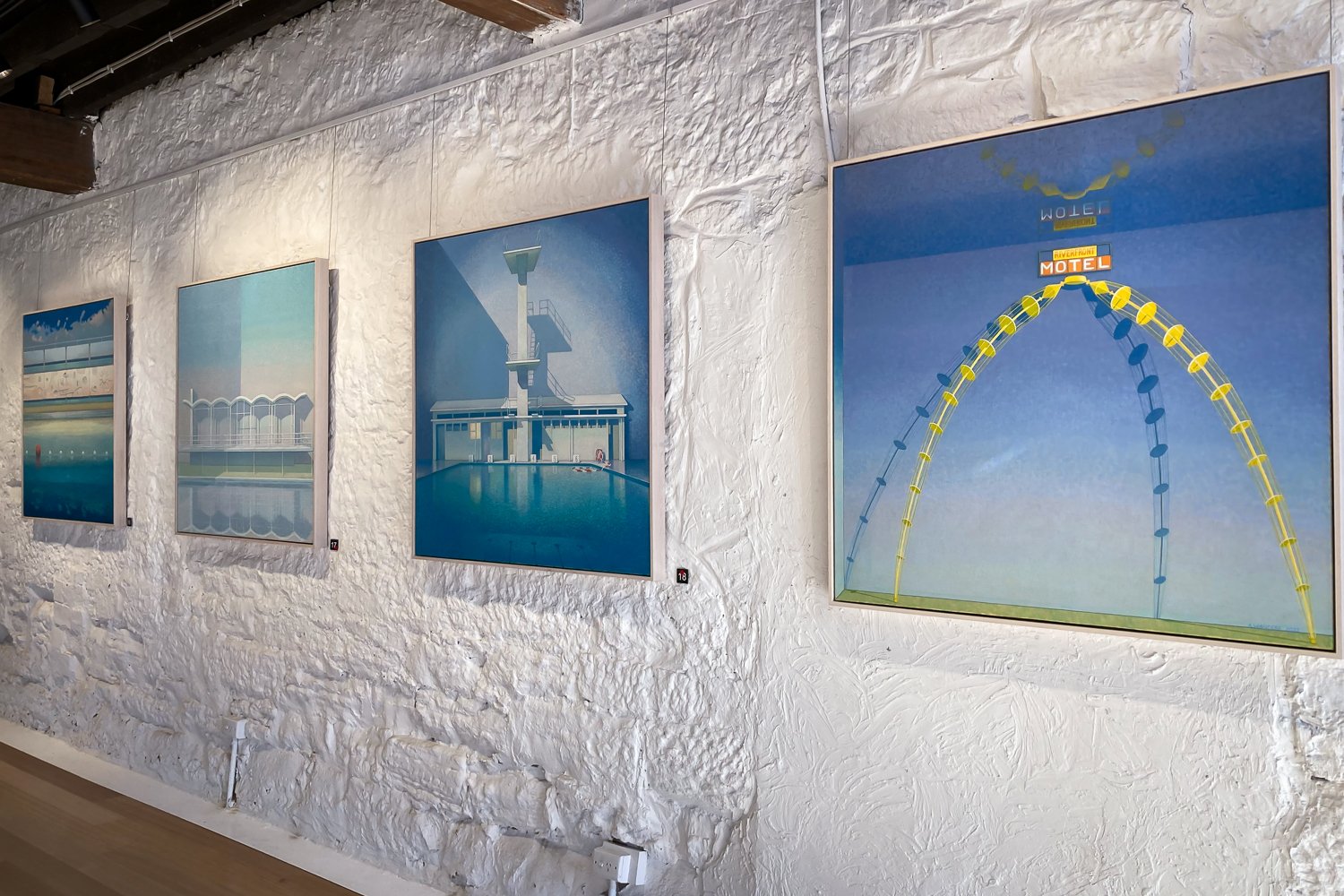 A row of paintings of modernist structures on a white textured gallery wall