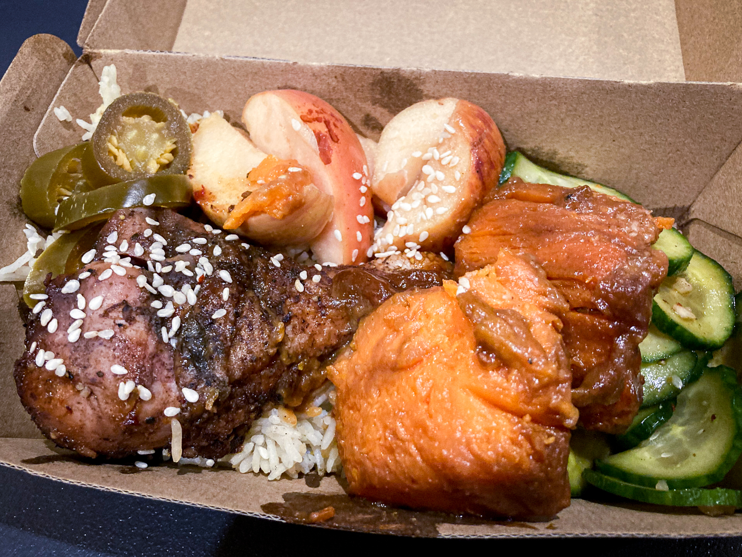 A food box containing spicy fried chicken, sweet potatoes, cooked apples, jalapenos, and cucumber side salad