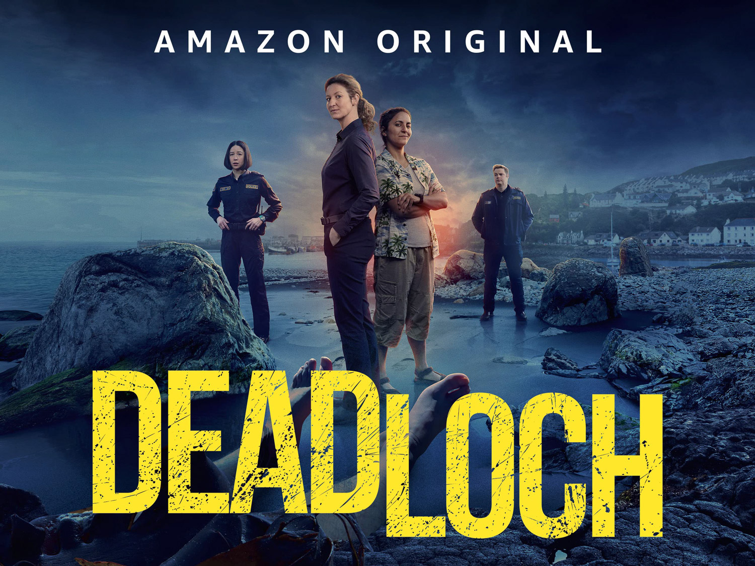Four people standing on a darkened beach with the word Deadloch in large yellow letters