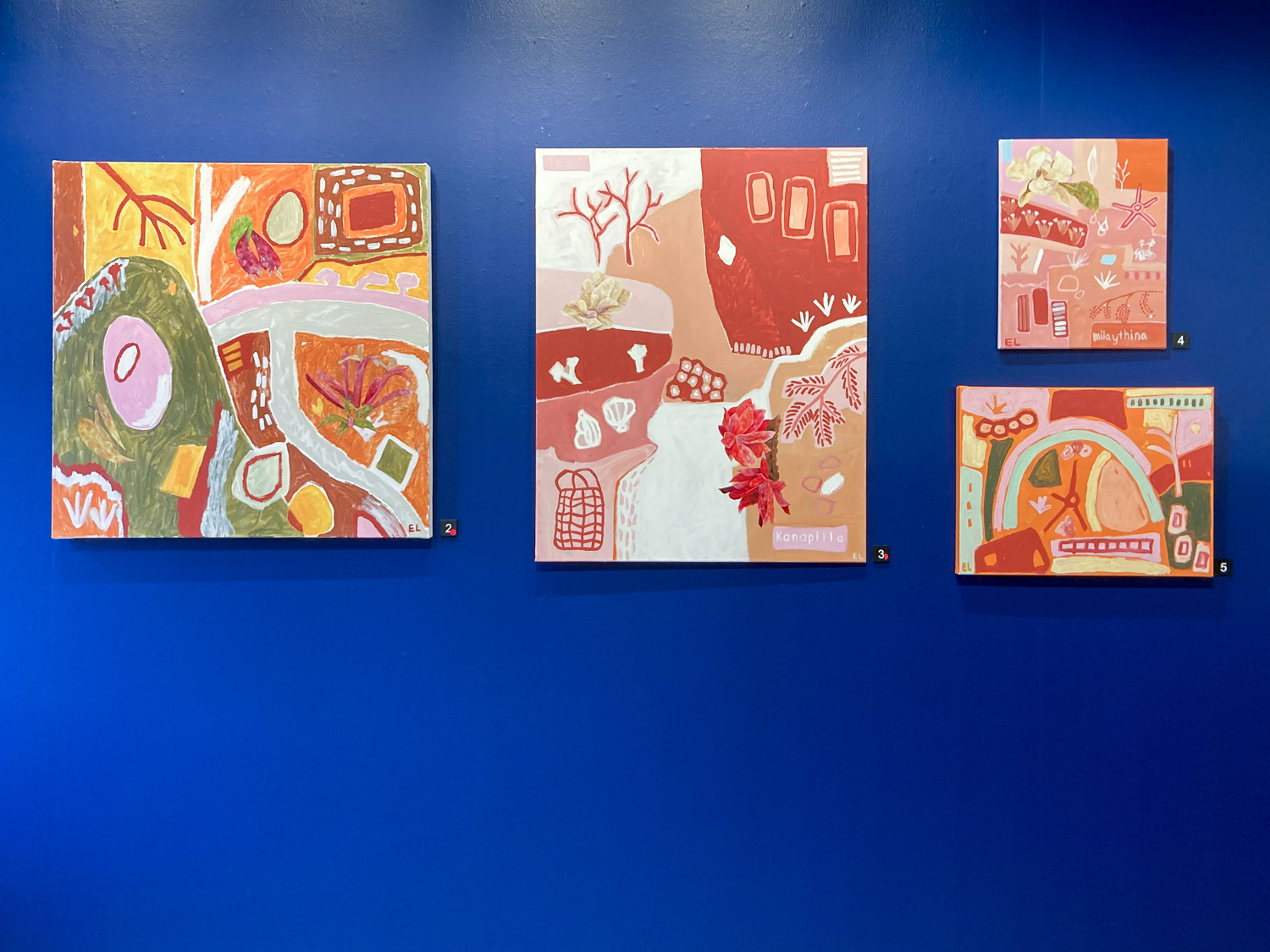 A series of four colourful paintings hung on a dark blue wall