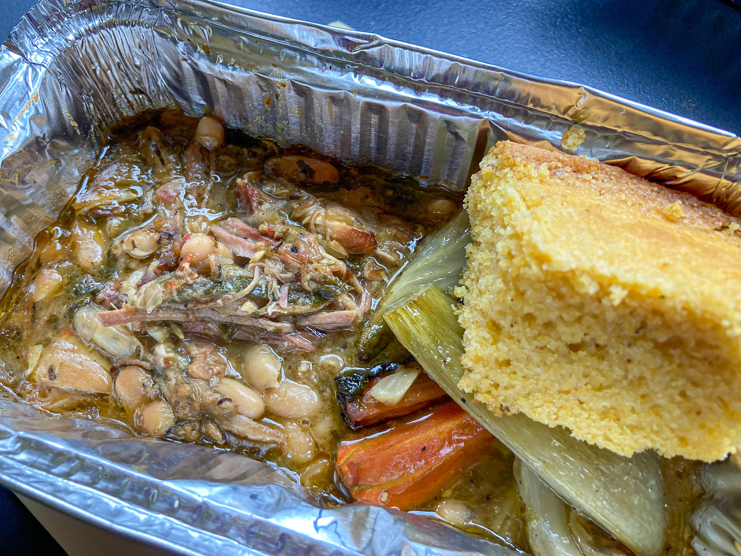 A foil dish with a stew of meat, white beans and vegetables topped with cornbread
