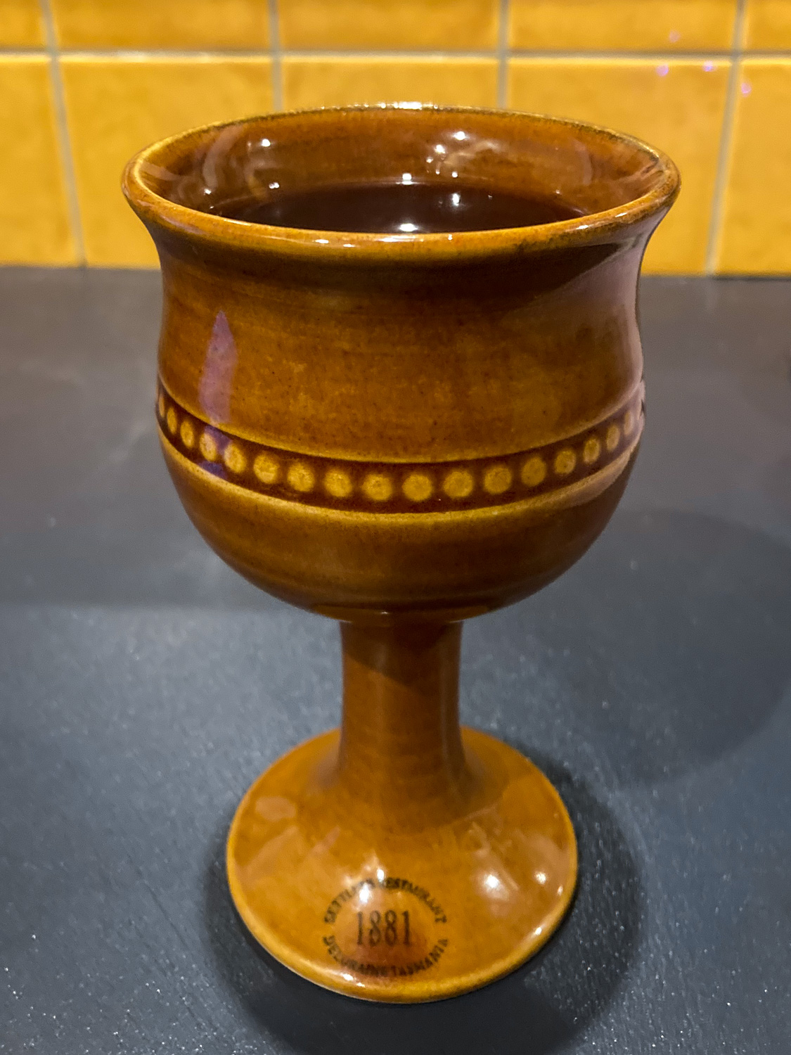 A light brown pottery wine goblet with a dark liquid inside