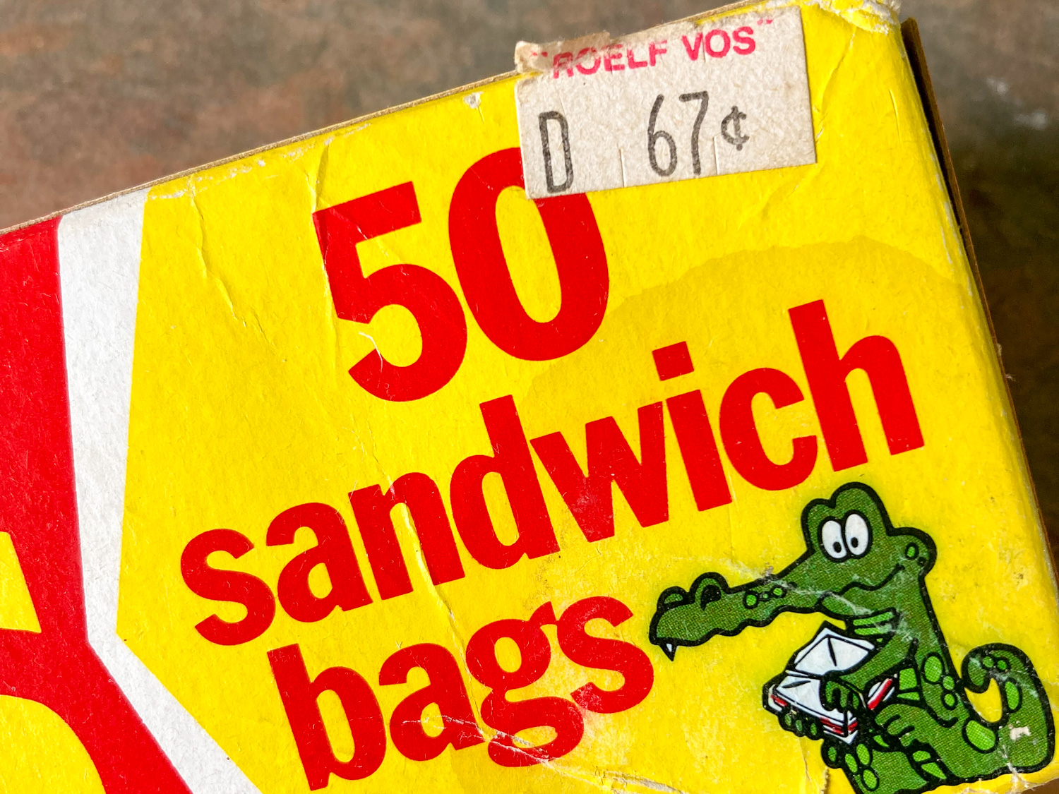 Part of a box, with red text on a yellow background stating "50 sandwich bags" with a picture of a cartoon alligator and a price sticker with the words ROELF VOS D 67c