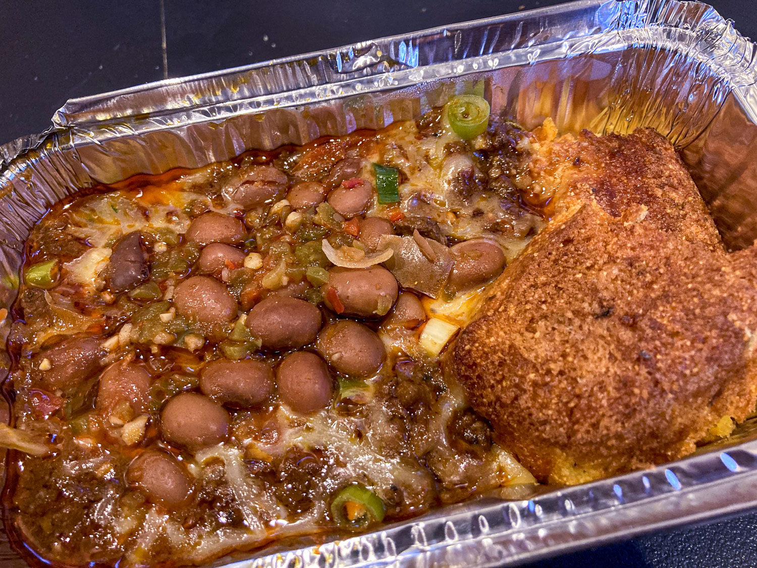 A foil container of beef chili with beans and cornbread
