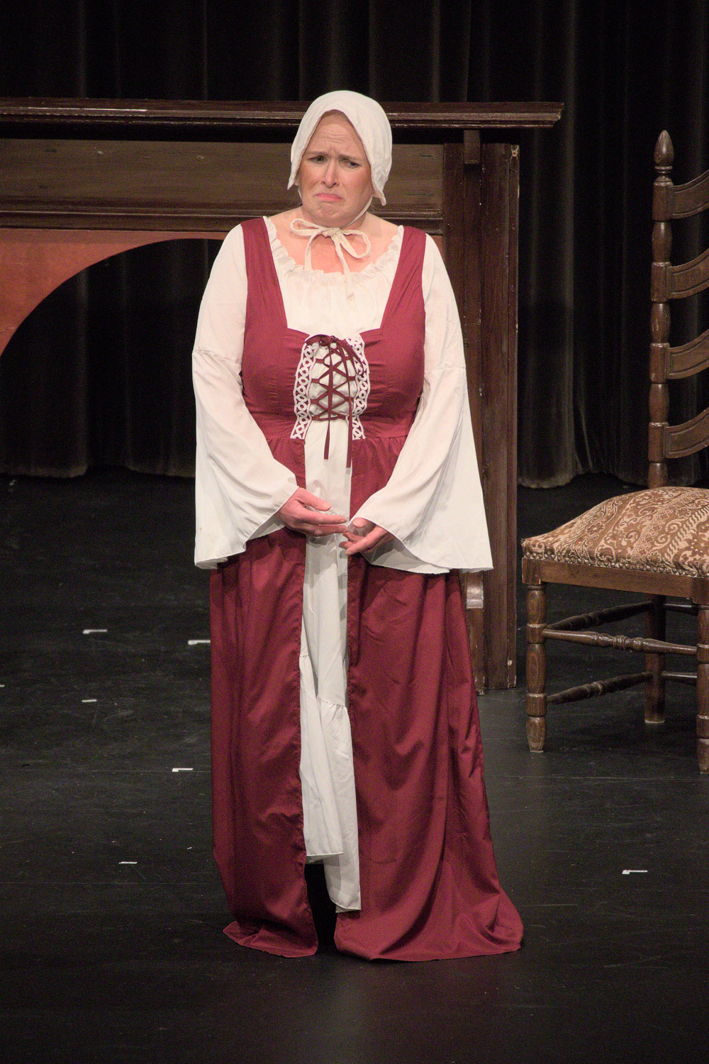 A woman on a stage dressed in a red and white medieval style gown with a white bonnet