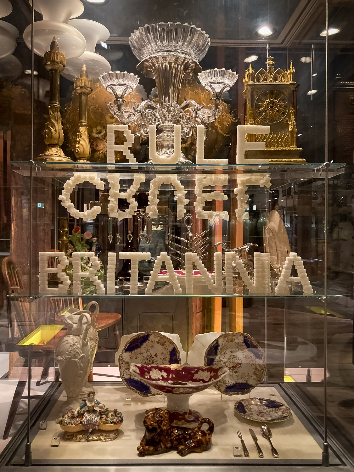 An artwork made from bread bearing the words RULE BRITANNIA with the word CRUEL upside down, all in a glass cabinet 