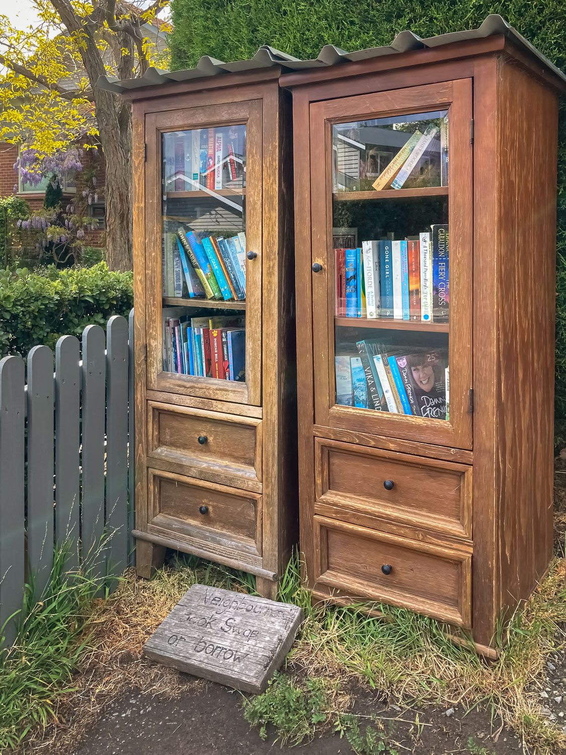 A wooden cupboard with glass doors and wooden drawers set up as a street library