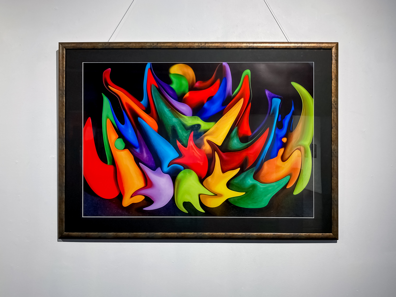 A photograph of bright colour splashes on a black background, hanging on a white wall