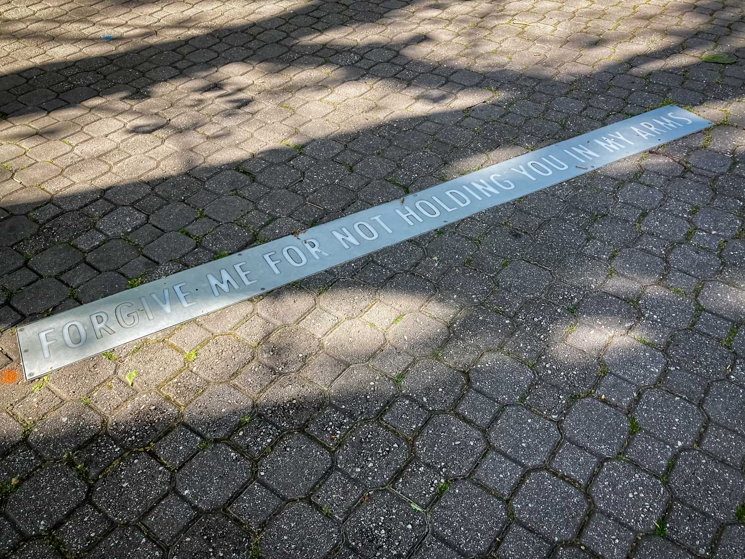 A strip of text across a tiled pavement bearing the words "Forgive me for not holding you in my arms"
