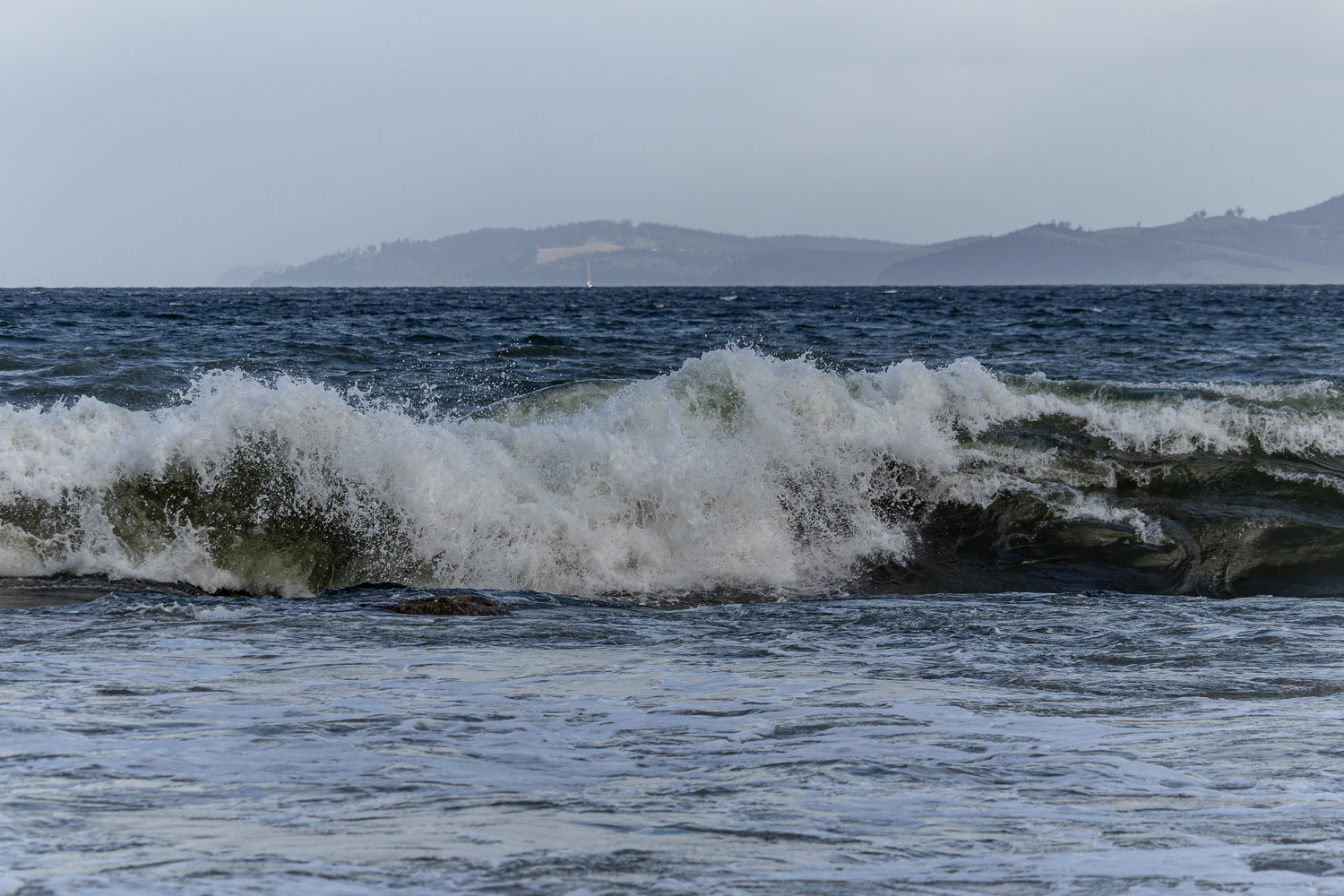 A foamy incoming wave in the water with hills in the background