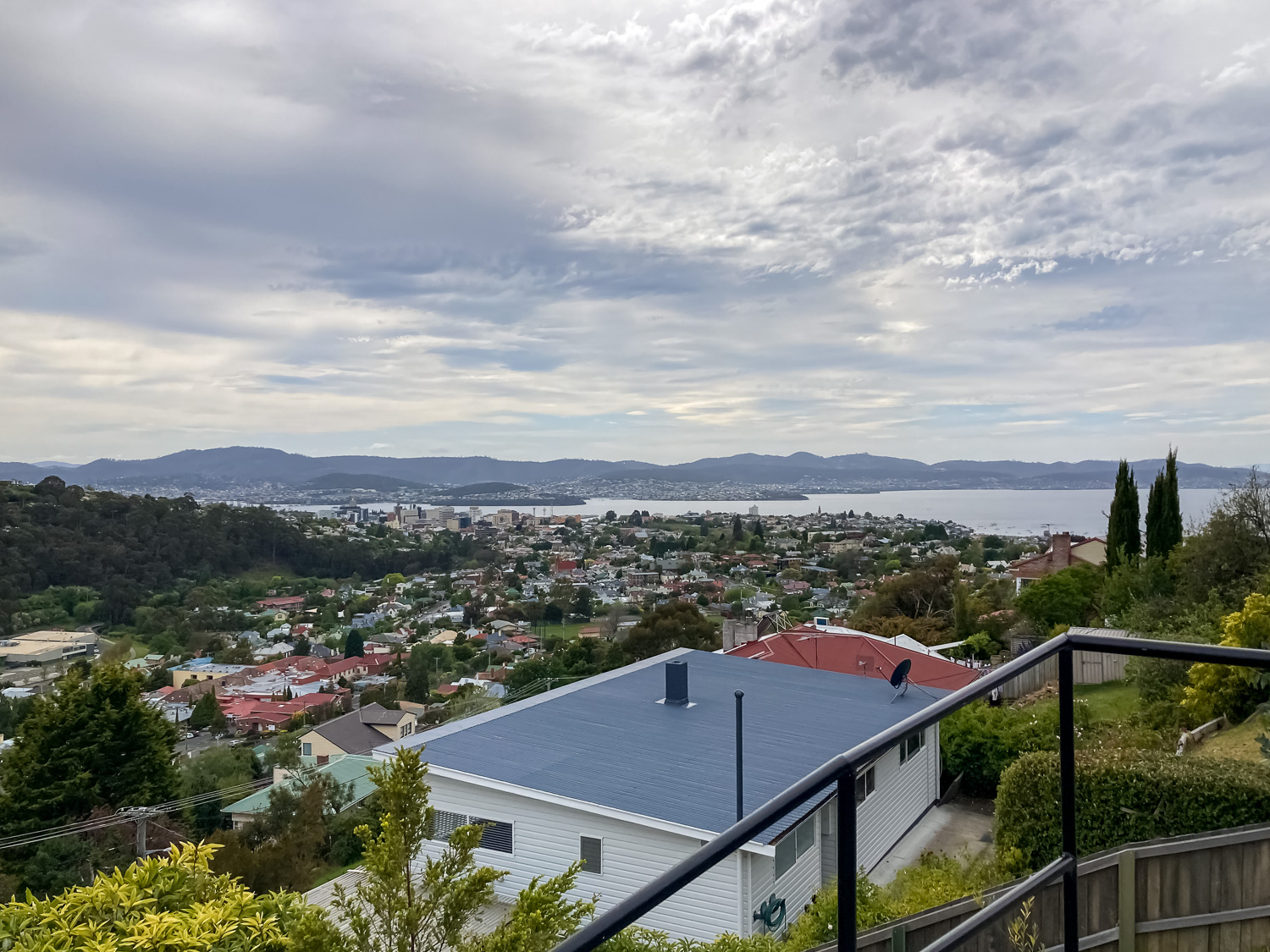 View overlooking Hobart with a white house and a rail in the foreground, the river and hills in the background