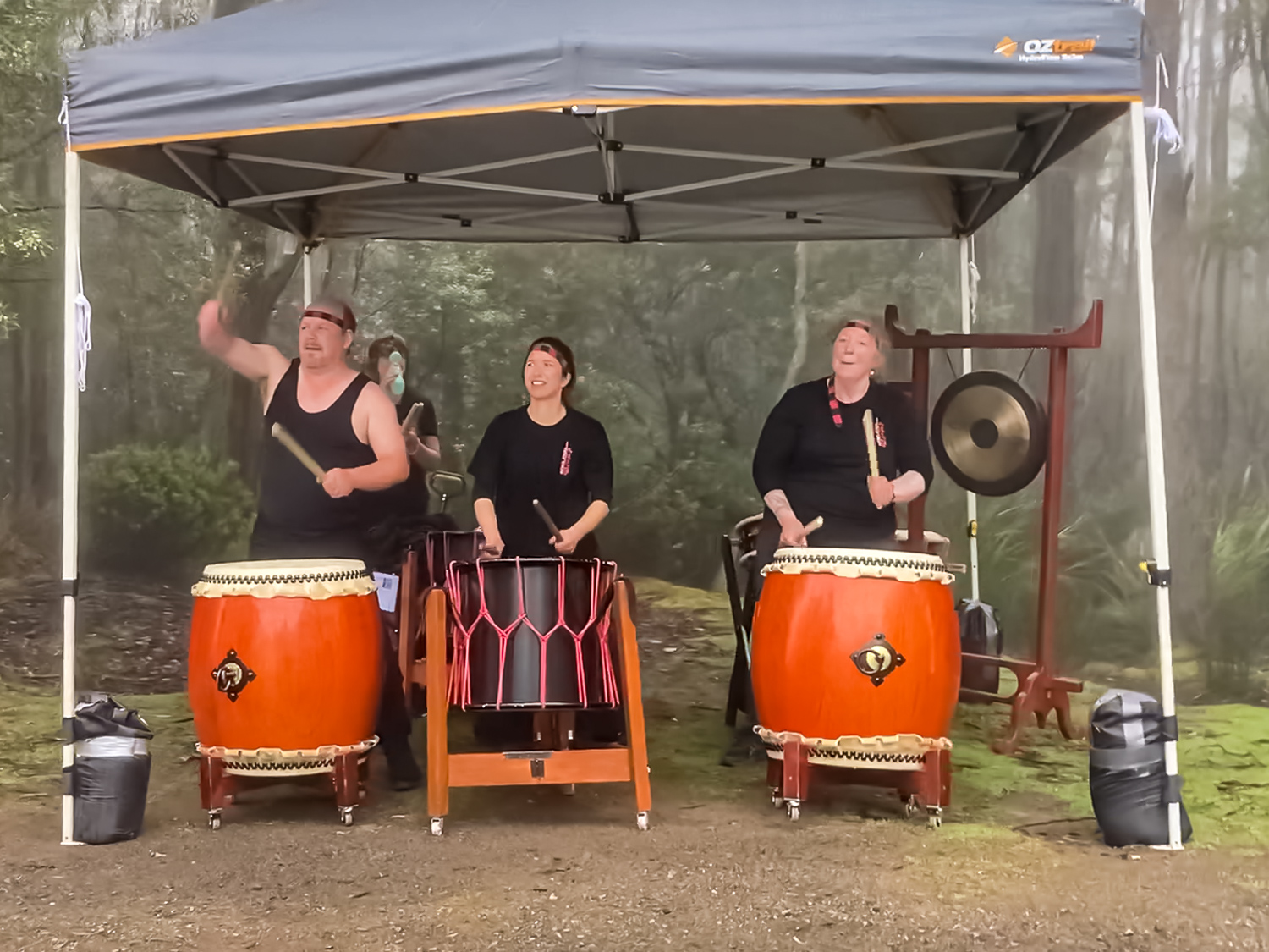 Three people playing large orange drums