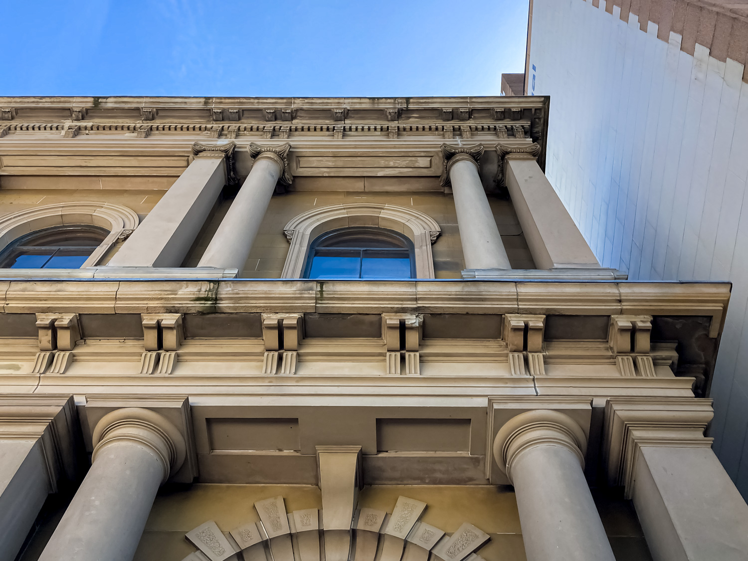 Looking up at a two-storey sandstone building with sets of round and square columns 
