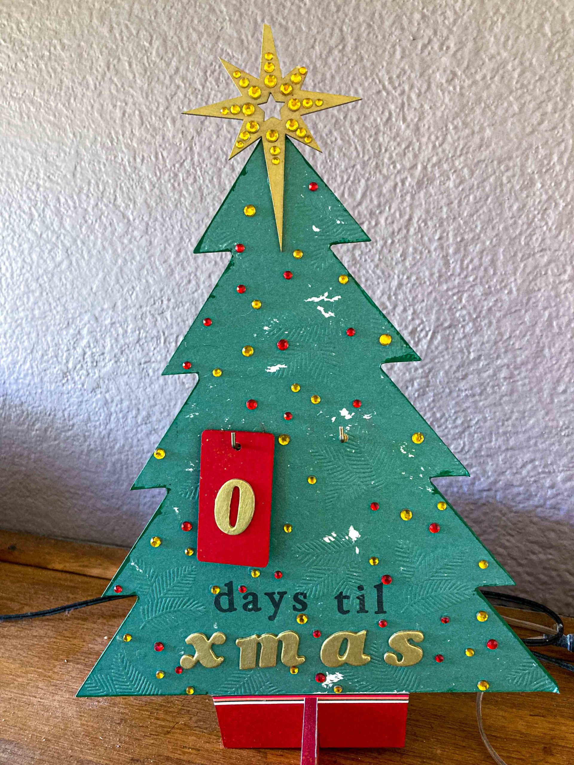 A battered wooden pine tree with a red 0 above the words 'days til xmas'. There is a broken gold wooden star on the top of the tree