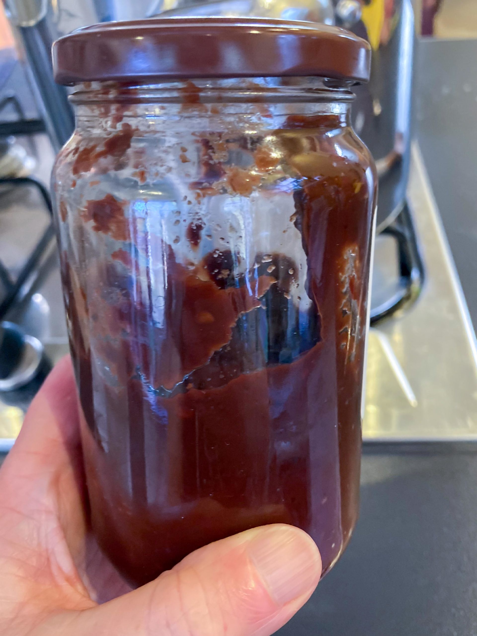 A hand holding a half-full jar of a red-brown sauce