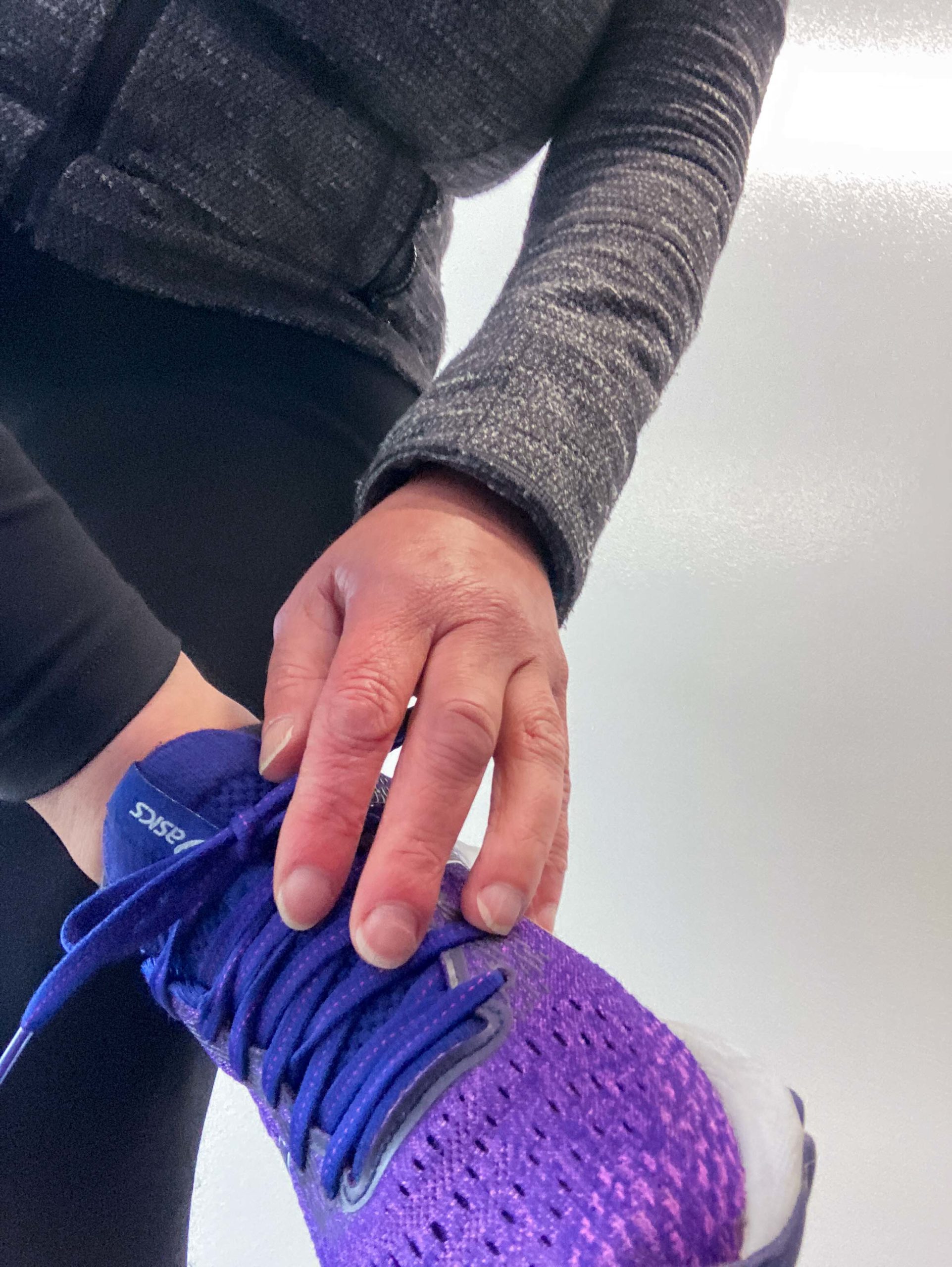 A foot in a purple running shoe being held off the ground with a hand on the shoelace