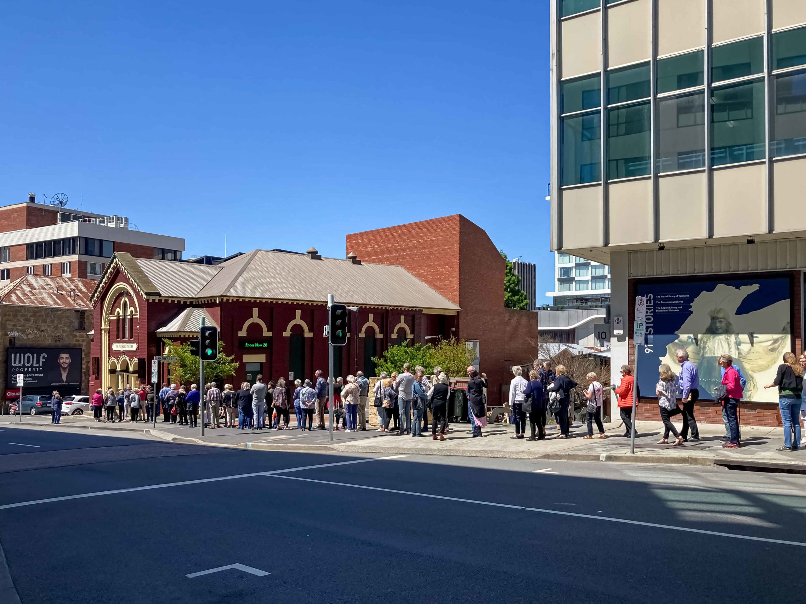 A line of people standing outside a dark red building called Playhouse Theatre