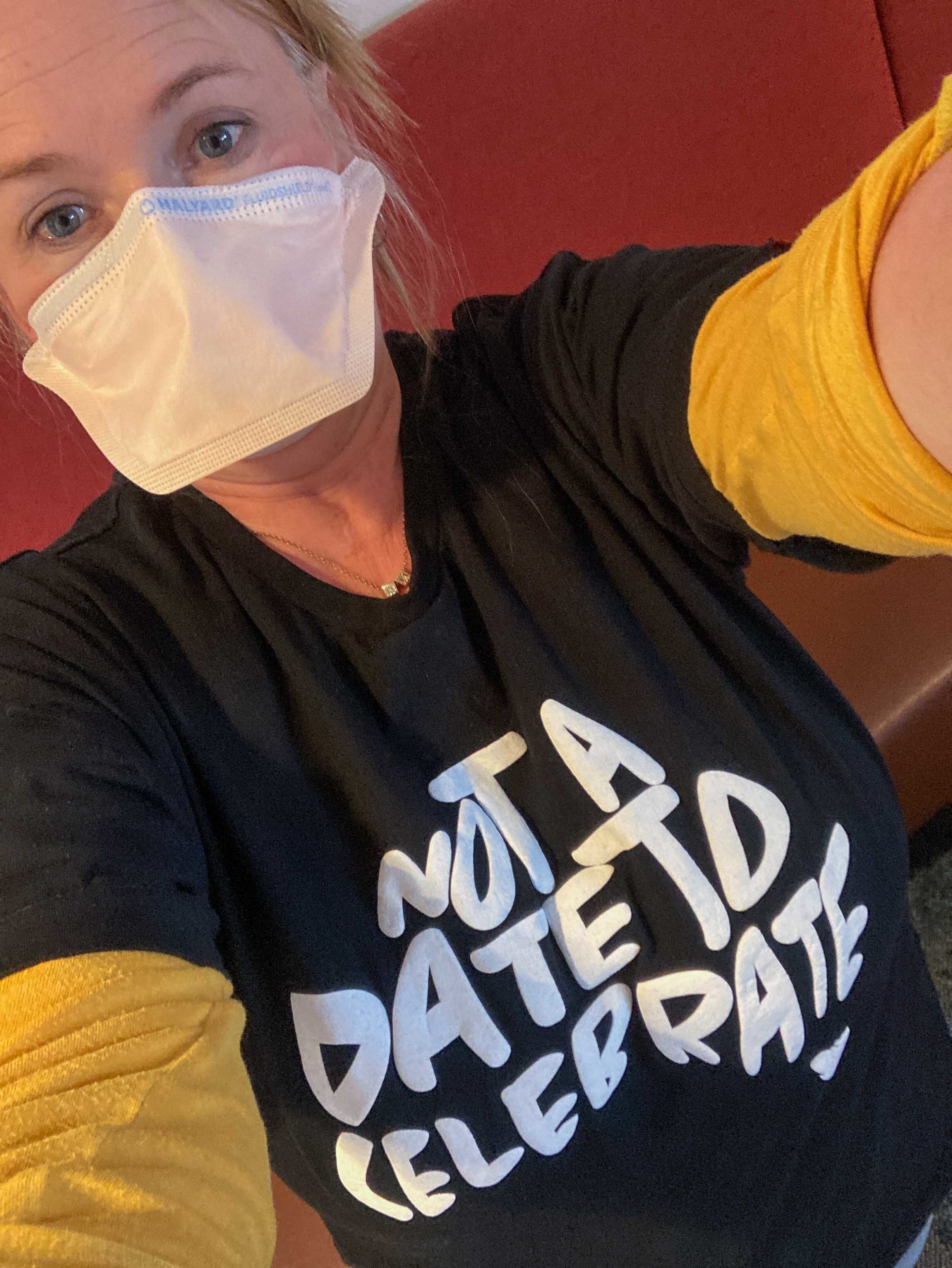 Barb is taking a selfy. She has a black t-shirt with the words "Not A Date To Celebrate" in the shape of Australia. She is wearing a face mask