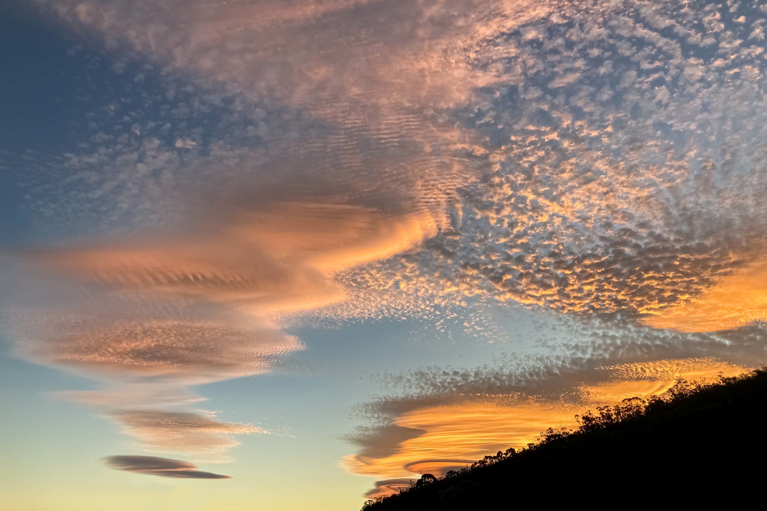 Pancake shaped clouds at sunset in formation over a tree-lined hill