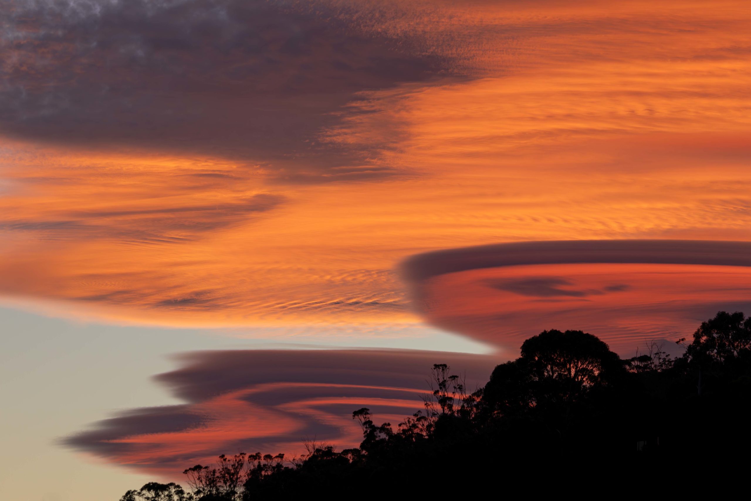 Rippled clouds resembling a pancake stack over a tree-lined hill at sunset