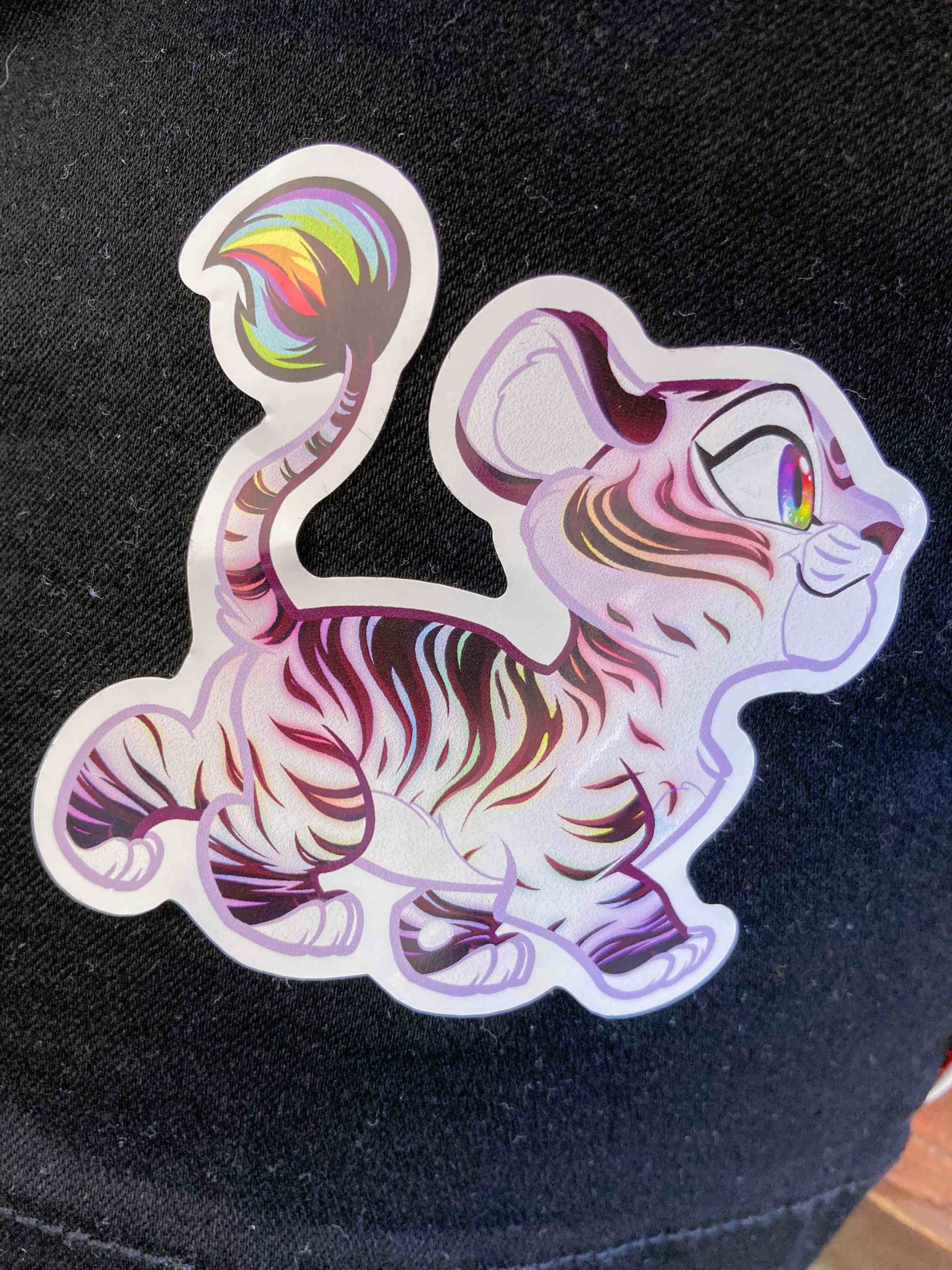 A rainbow pride little lion sticker stuck onto black clothing