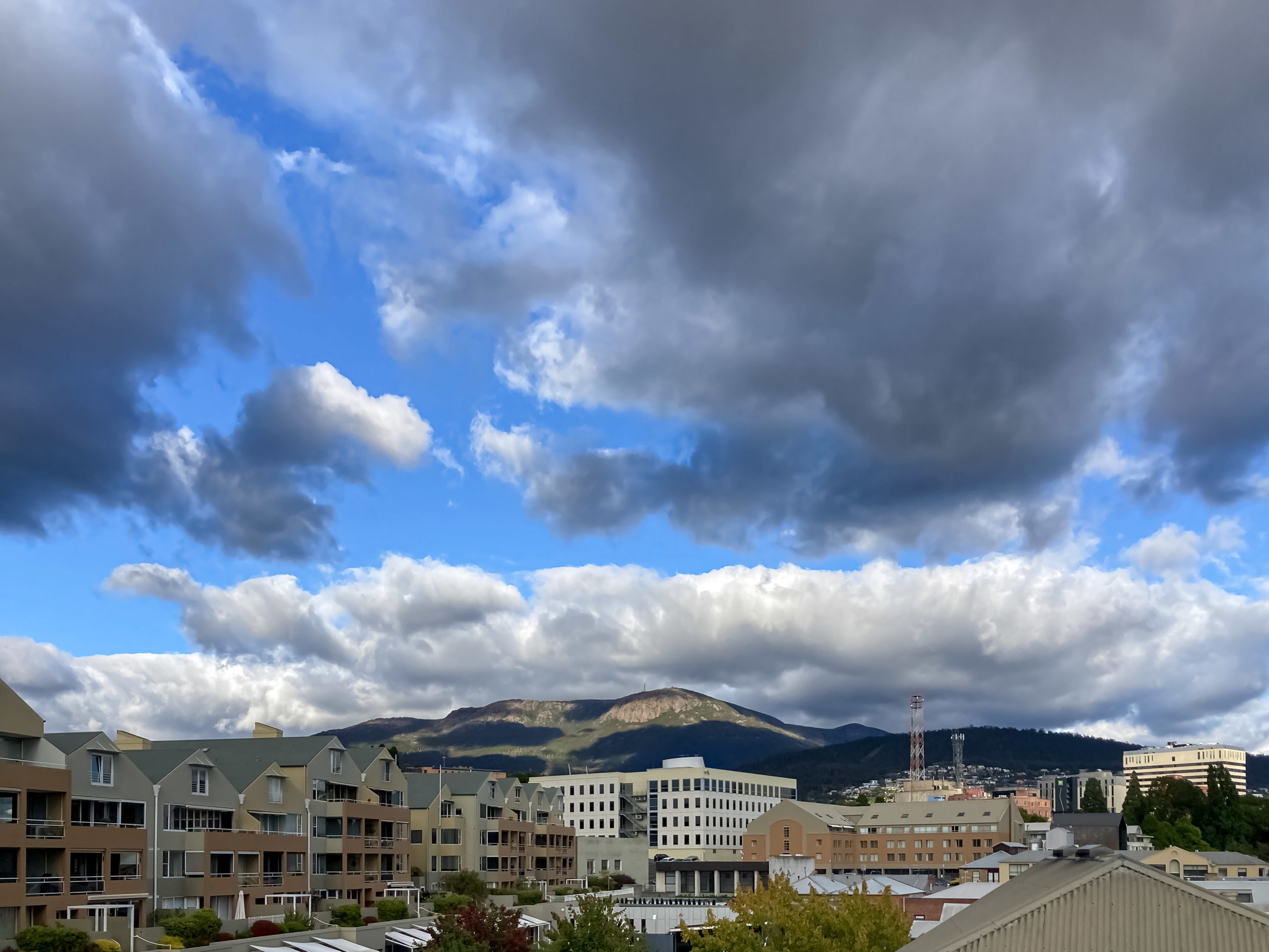 A blue, cloudy morning sky with a mountain in the background and buildings in the foreground
