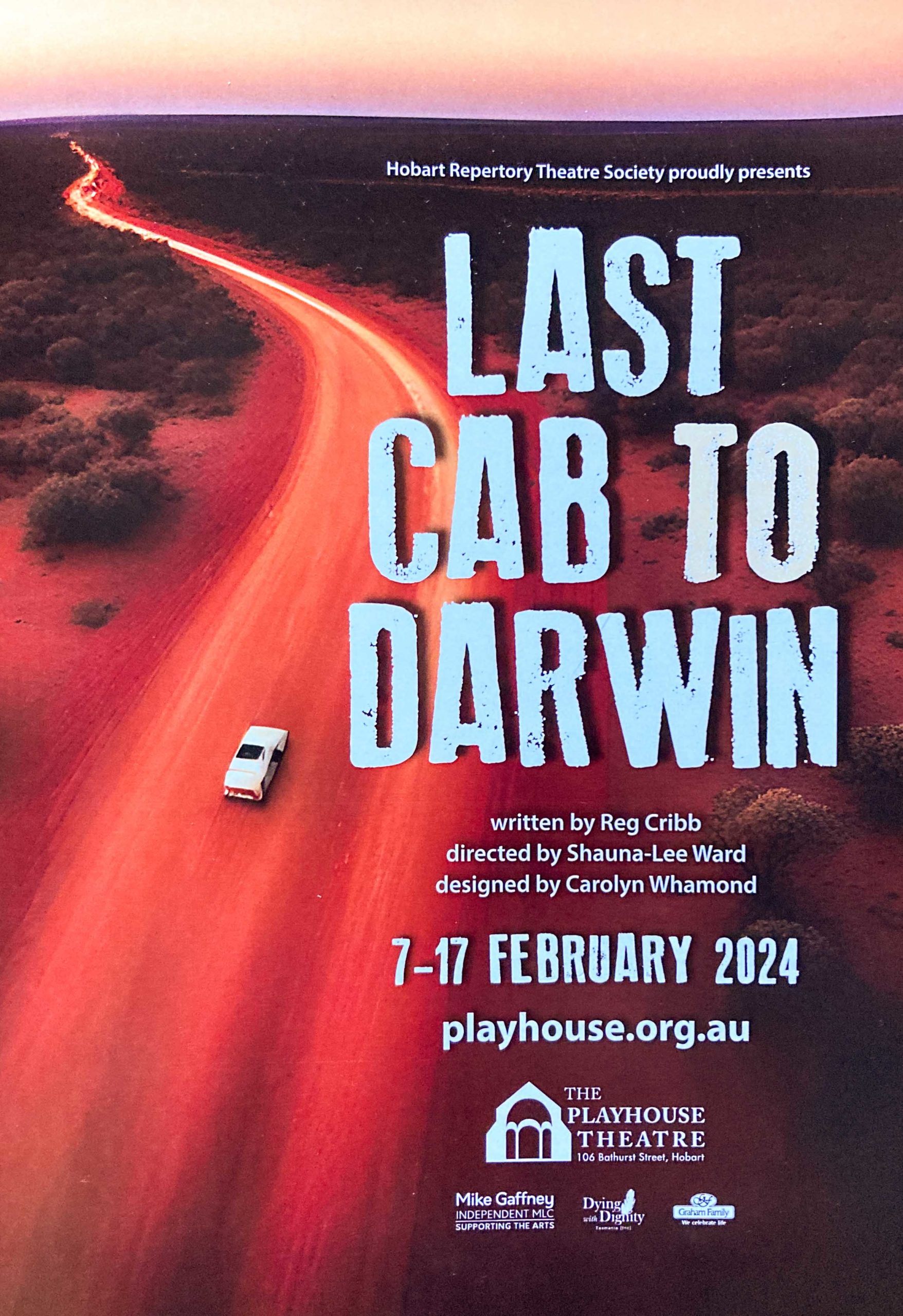 An aerial shot of a car driving on a long red road, with the words LAST CAB TO DARWIN prominent on the right hand side of the picture
