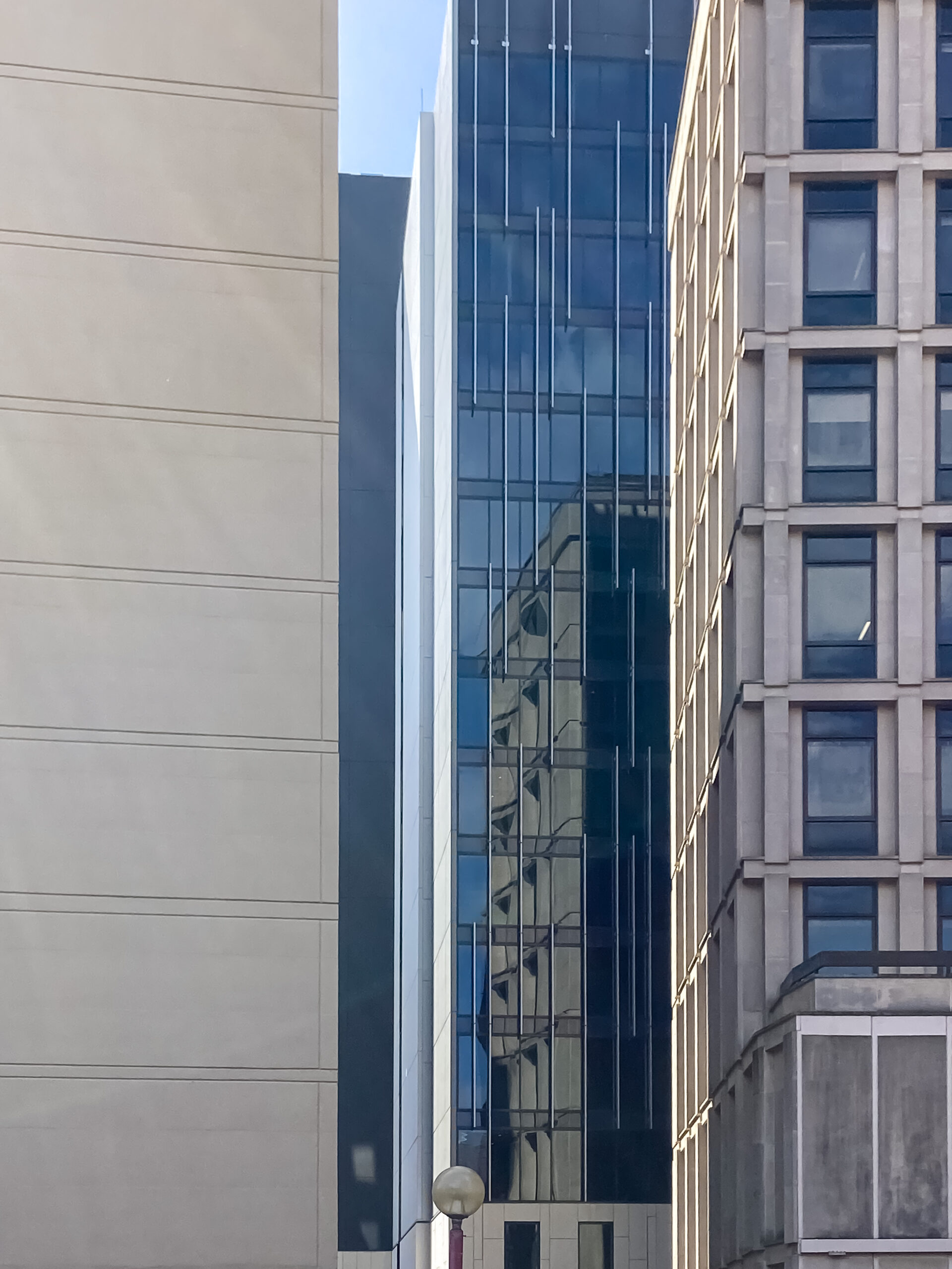 A tall brutalist building reflected in the glass wall of a nearby tall building