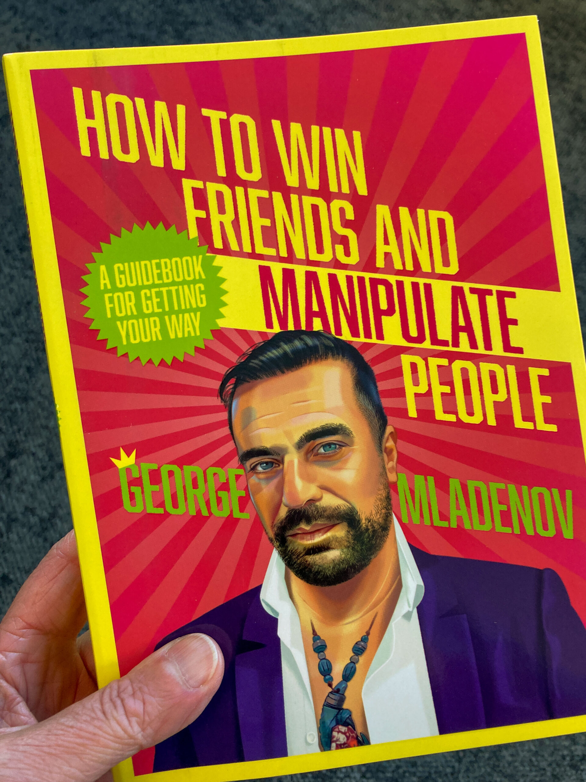 A pink book cover featuring a picture of a bearded man and the words in yellow uppercase letters HOW TO WIN FRIENDS AND MANIPULATE PEOPLE - George Mladenov